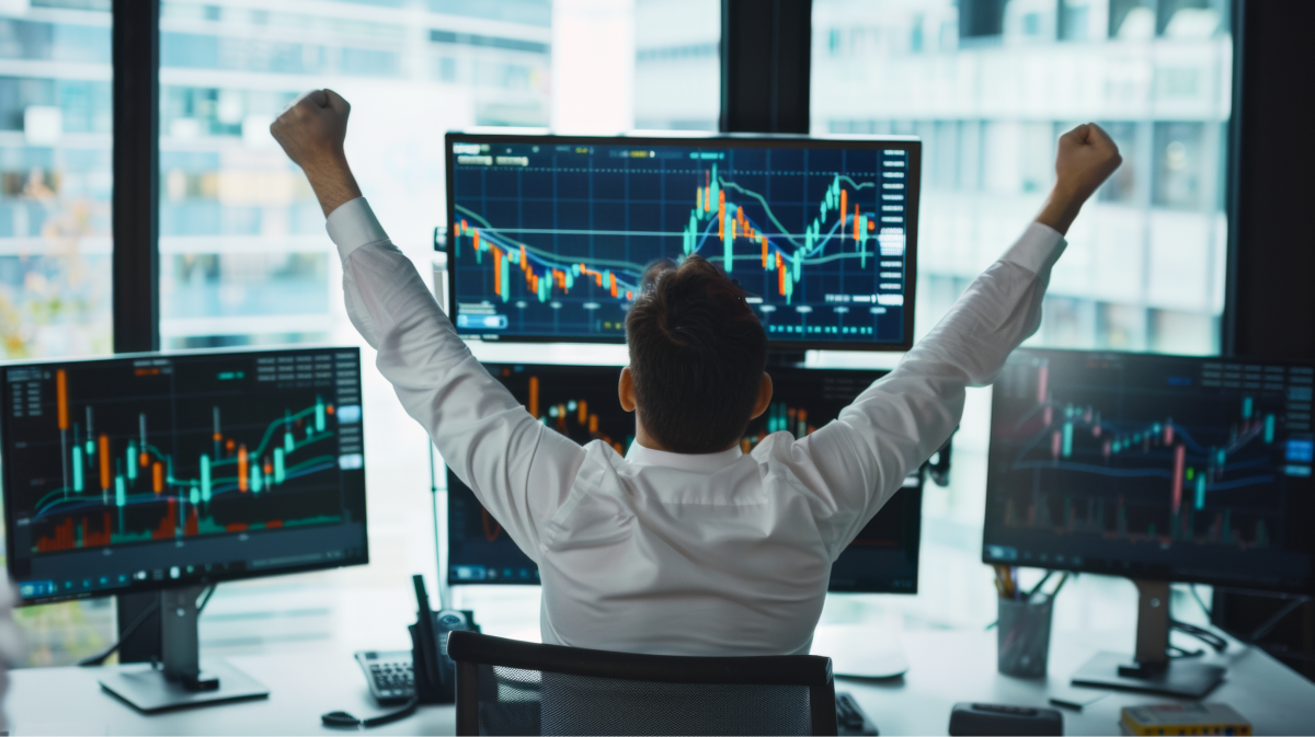 A trader celebrating a profitable session, excitedly raising his fist in front of multiple monitors displaying real-time market charts and indicators.