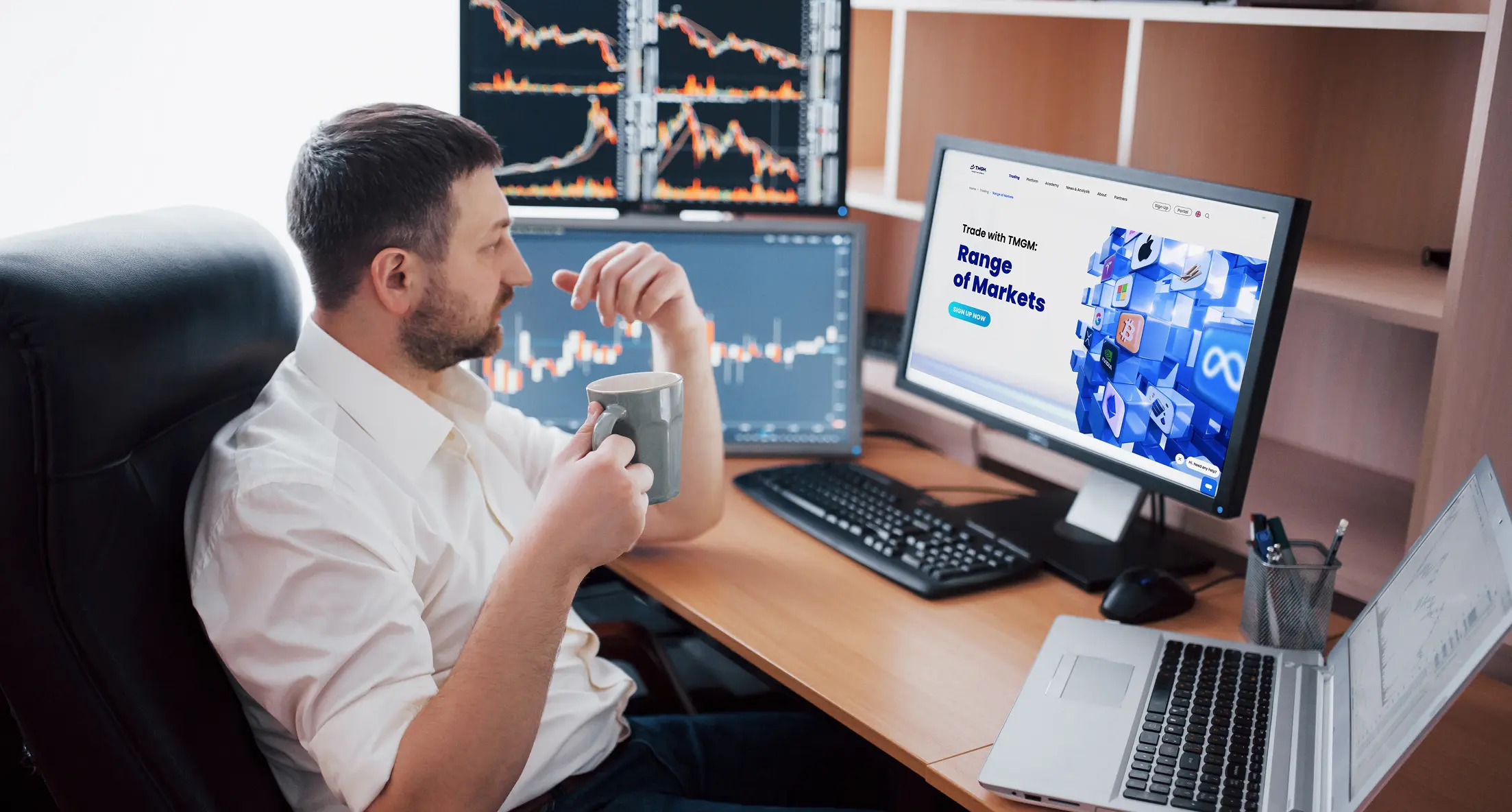 Trader at desk holding a mug while watching multiple candlestick charts and a TMGM range of markets page, illustrating a CFD trading workstation